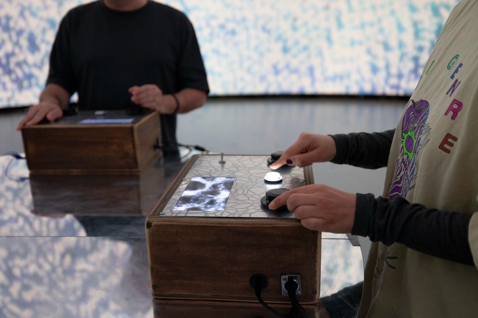 Hands on the knobs and buttons of two wooden controllers